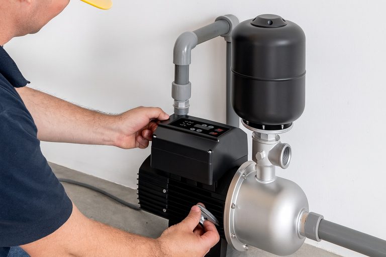 A professional technician (face not visible) adjusts a RAFSUN VFD Booster Pump installed in a clean home utility room. The sleek stainless steel and black pump is connected to grey PVC pipes and a compact pressure tank, demonstrating its role in stabilizing and increasing domestic water pressure efficiently. The bright, realistic lighting highlights the product’s durable design, energy-saving motor, and modern automatic control system — ideal for residential pressure-boosting applications.